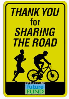 Yellow road-safety sign reading “Thank you for sharing the road” with a runner and cyclist silhouette.