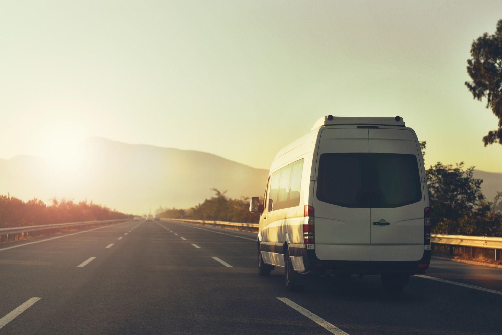 Una camioneta blanca circula por una autopista al atardecer.