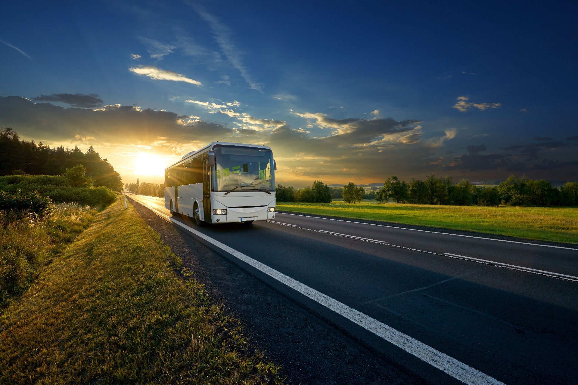 Un autobús circula por una carretera rural al atardecer.