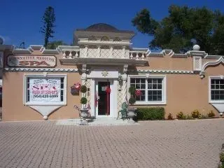 Small peach storefront with a red door, white trim, hanging flowers, and a paved courtyard.