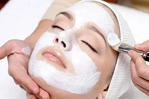 Facial mask being applied to a woman’s face with a brush in a spa treatment