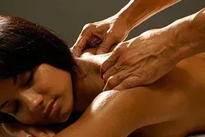 Massage therapist kneading a person’s shoulder and upper back in a warm, dimly lit setting