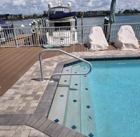 Pool with steps, handrail, and boat dock in the background. Blue water, tan decking.
