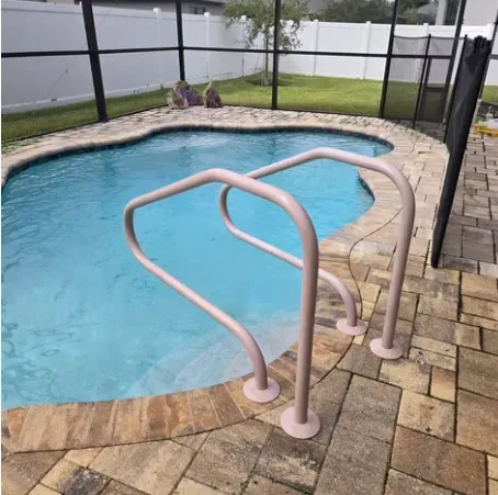 Pool with pink handrails on a brick patio, enclosed by a black fence and green lawn.