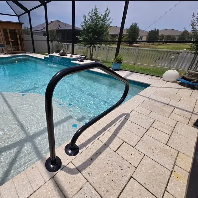 Black pool handrail next to a pool with turquoise water and stone pavers.