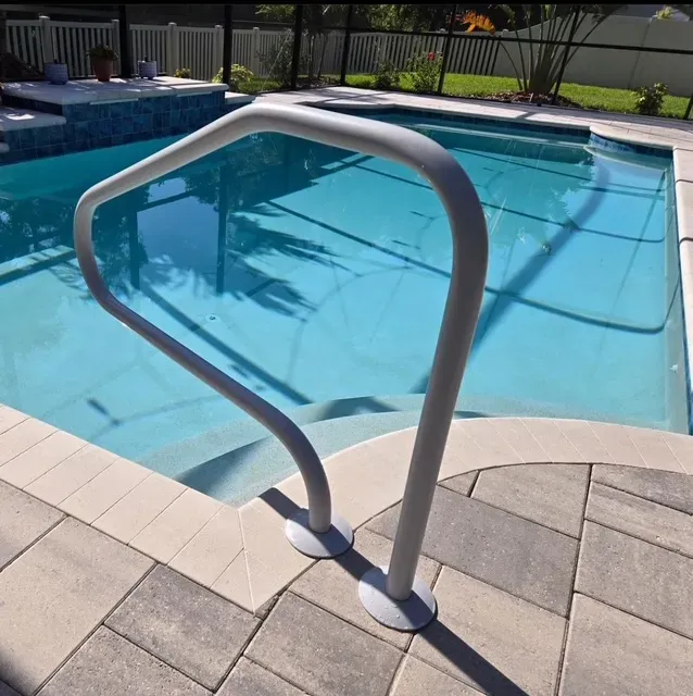 Pool with steps, light gray handrail, and gray and beige tile surround. Sunny outdoor setting.