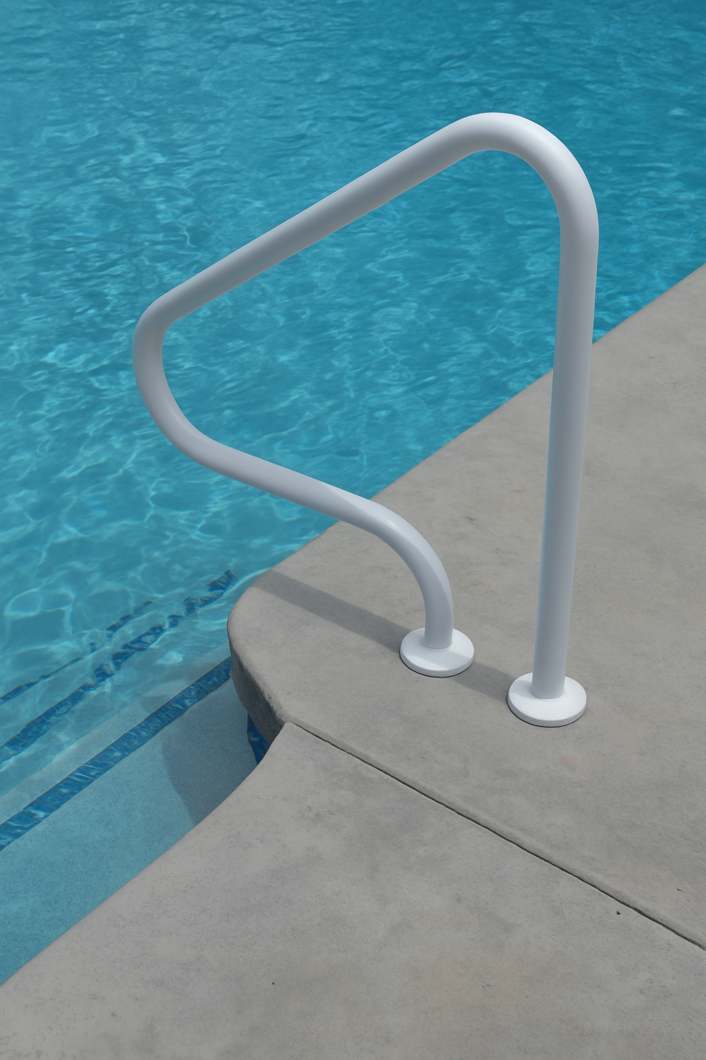 A kidney-shaped swimming pool with a surrounding stone patio, surrounded by a black fence. Trees and greenery are in the background.
