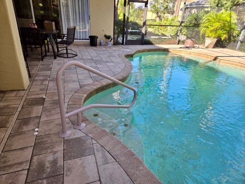 Pool area with paved patio and water, handrail.