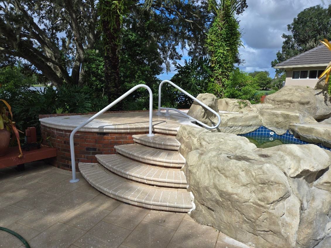 Steps leading to a hot tub with a white handrail, next to a rock formation and trees.