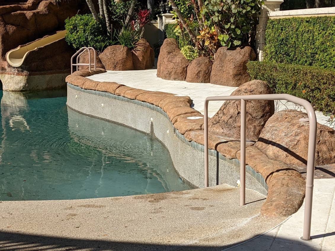 Poolside with a slide, rock formations, and a water view.