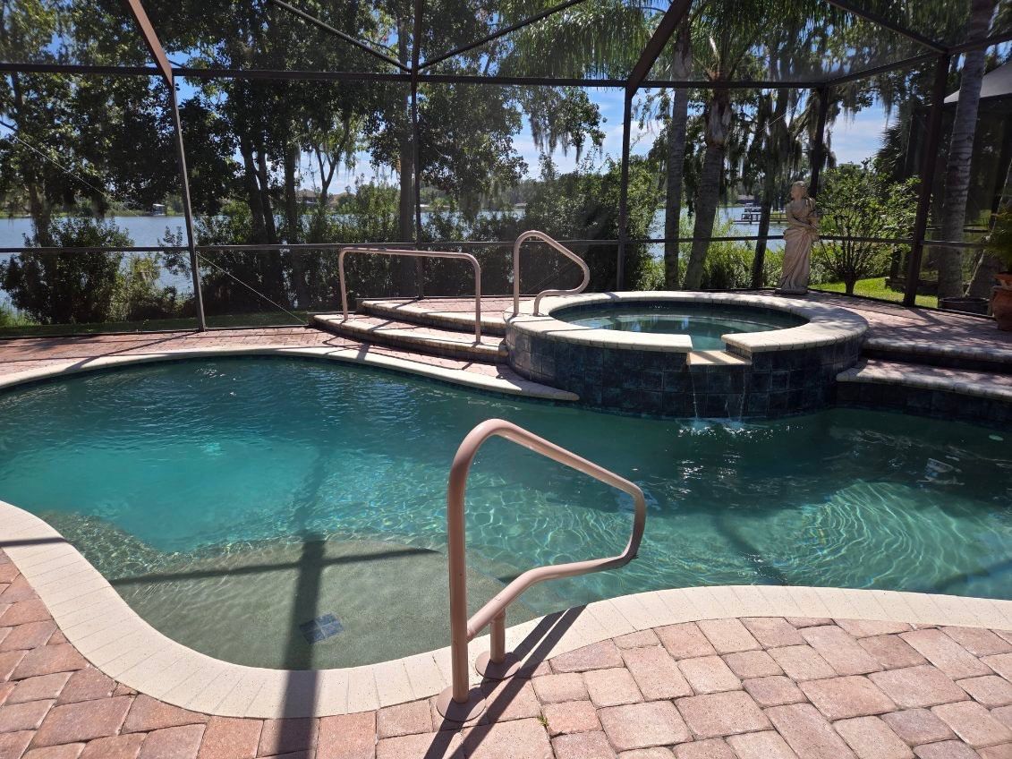Pool and hot tub with a brick patio, fenced with a lake in the background.