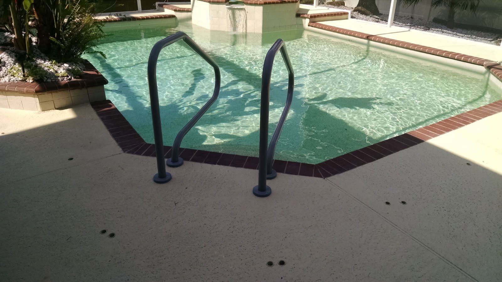 Pool with ladder and surrounding patio. Green water, dark metal ladder, and brick border.