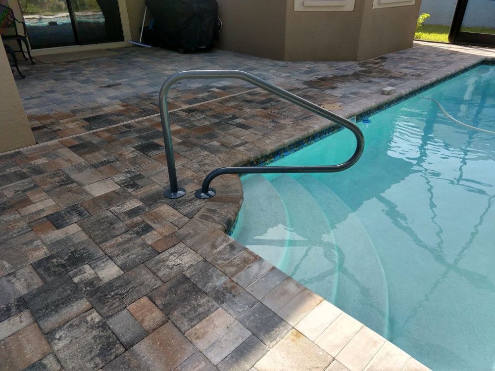 Pool with steps and handrail, surrounded by brick pavers.