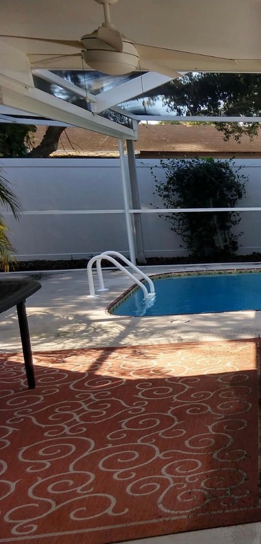 A pool area with a blue pool, white pool ladder, and red rug.