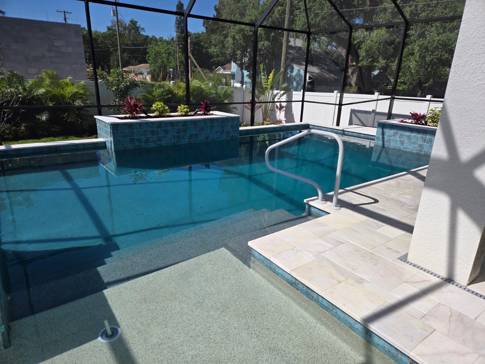 Pool with built-in steps and jacuzzi, surrounded by a screen enclosure, blue water, and light-colored tiling.