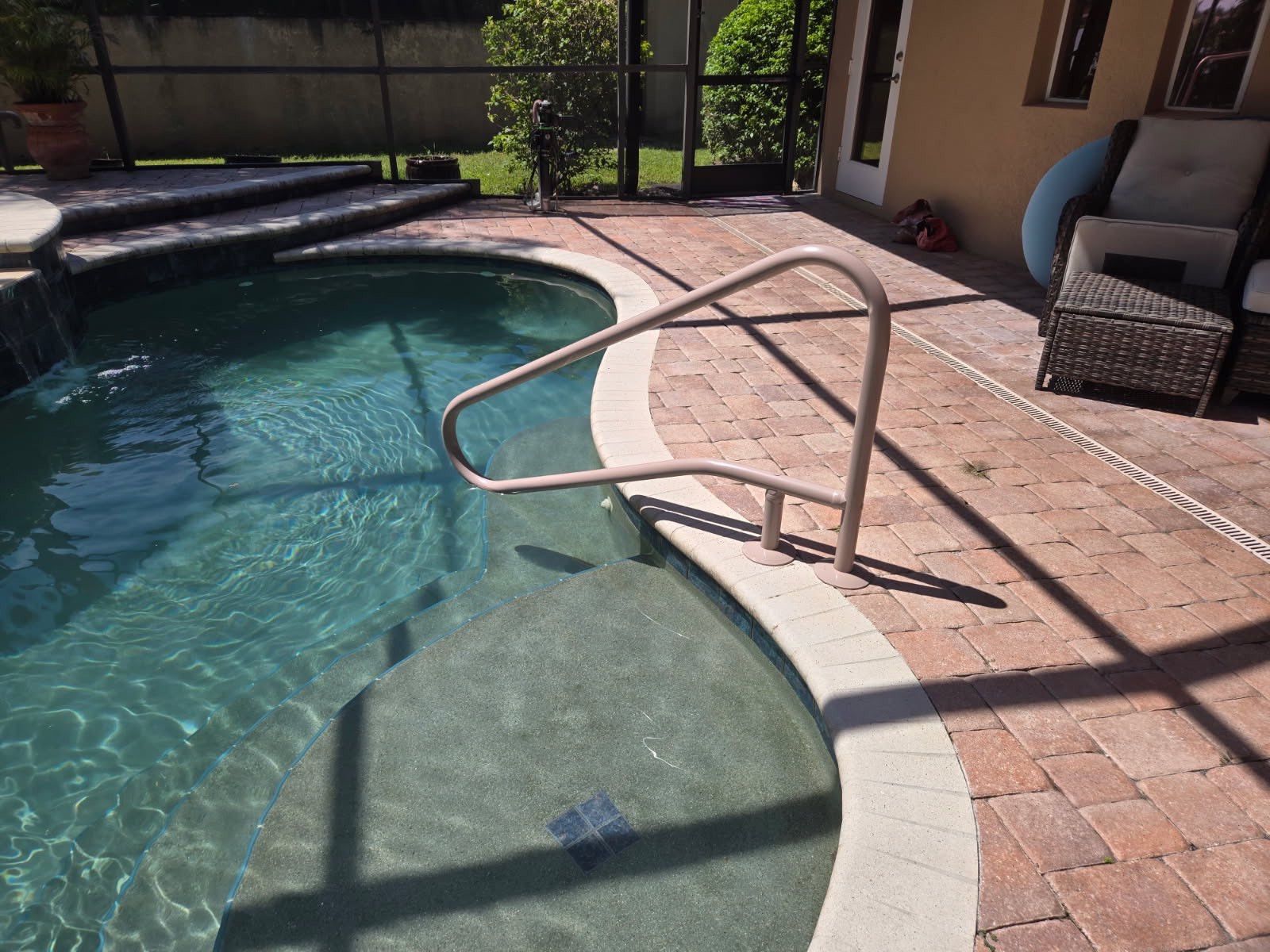 Swimming pool with a handrail, steps, and patio. Brown brick surround, clear water.