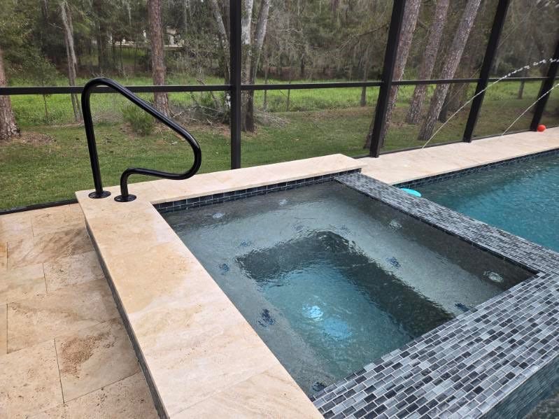 A built-in jacuzzi next to a pool, with a handrail for accessibility, outdoors.