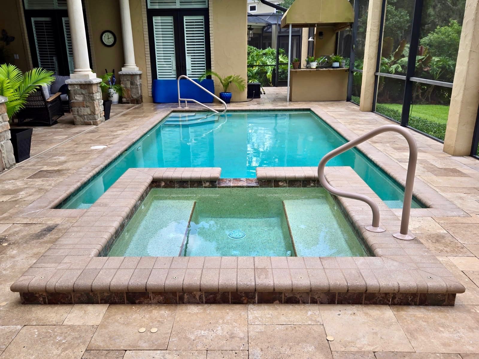 A pool with a connected spa, tan stonework, and an outdoor patio.