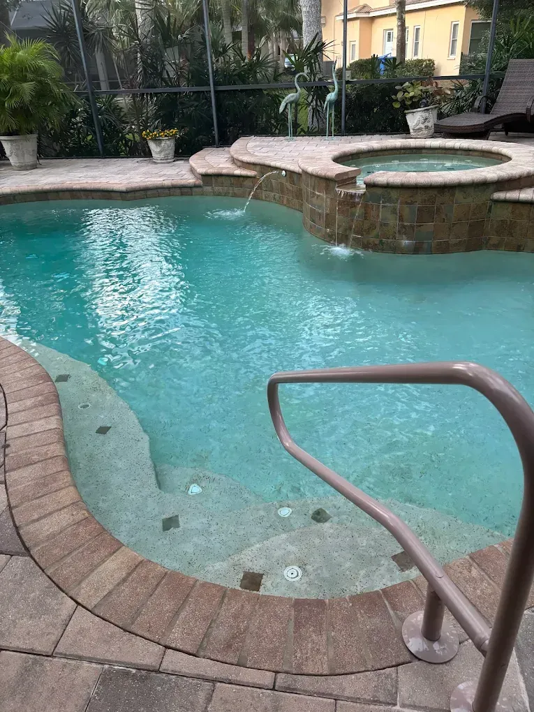 A swimming pool with turquoise water and a small spa. A metal handrail is visible.