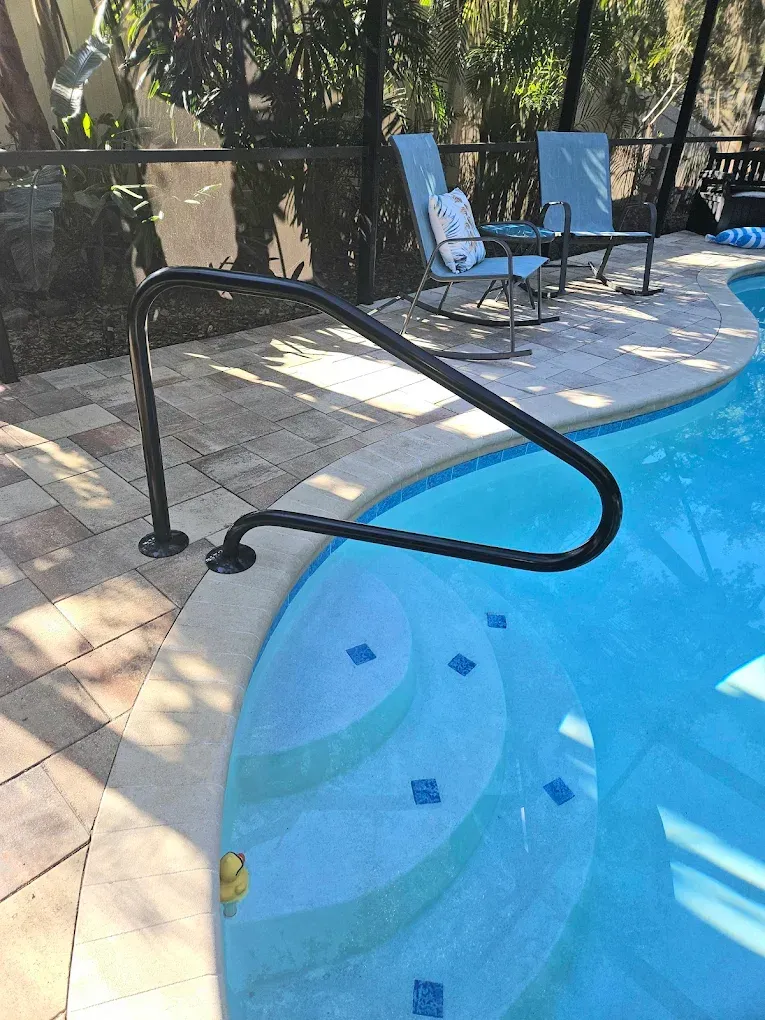 Black pool handrail at the edge of a swimming pool with light blue water and stairs.