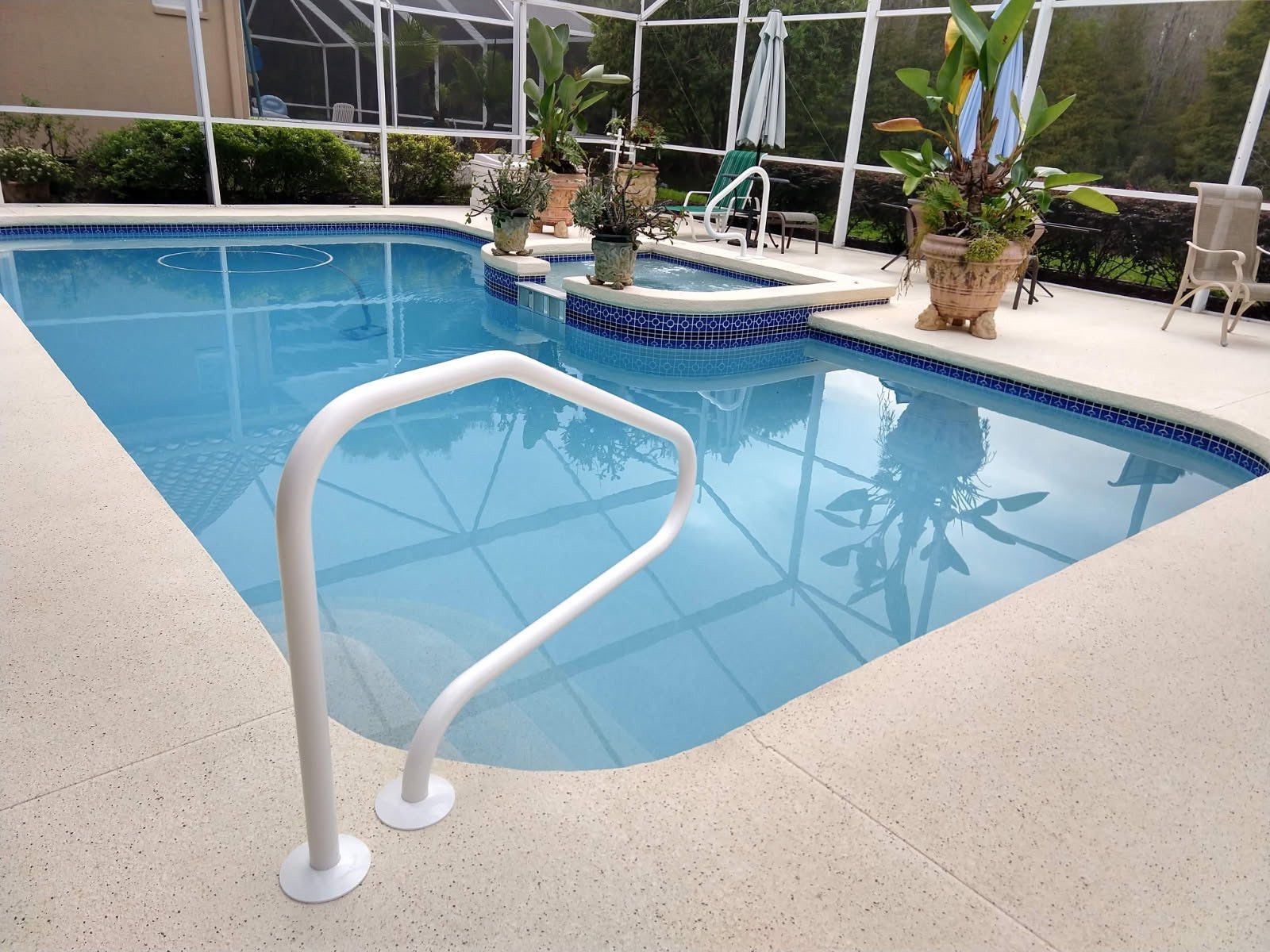 Pool with blue water, white handrail, and beige patio; plants in pots surround.