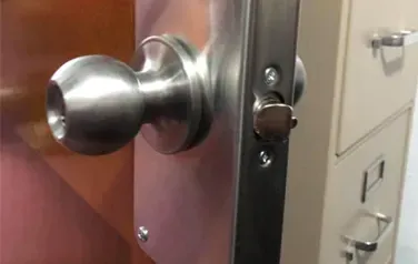 A close up of a door knob on a door next to a filing cabinet.