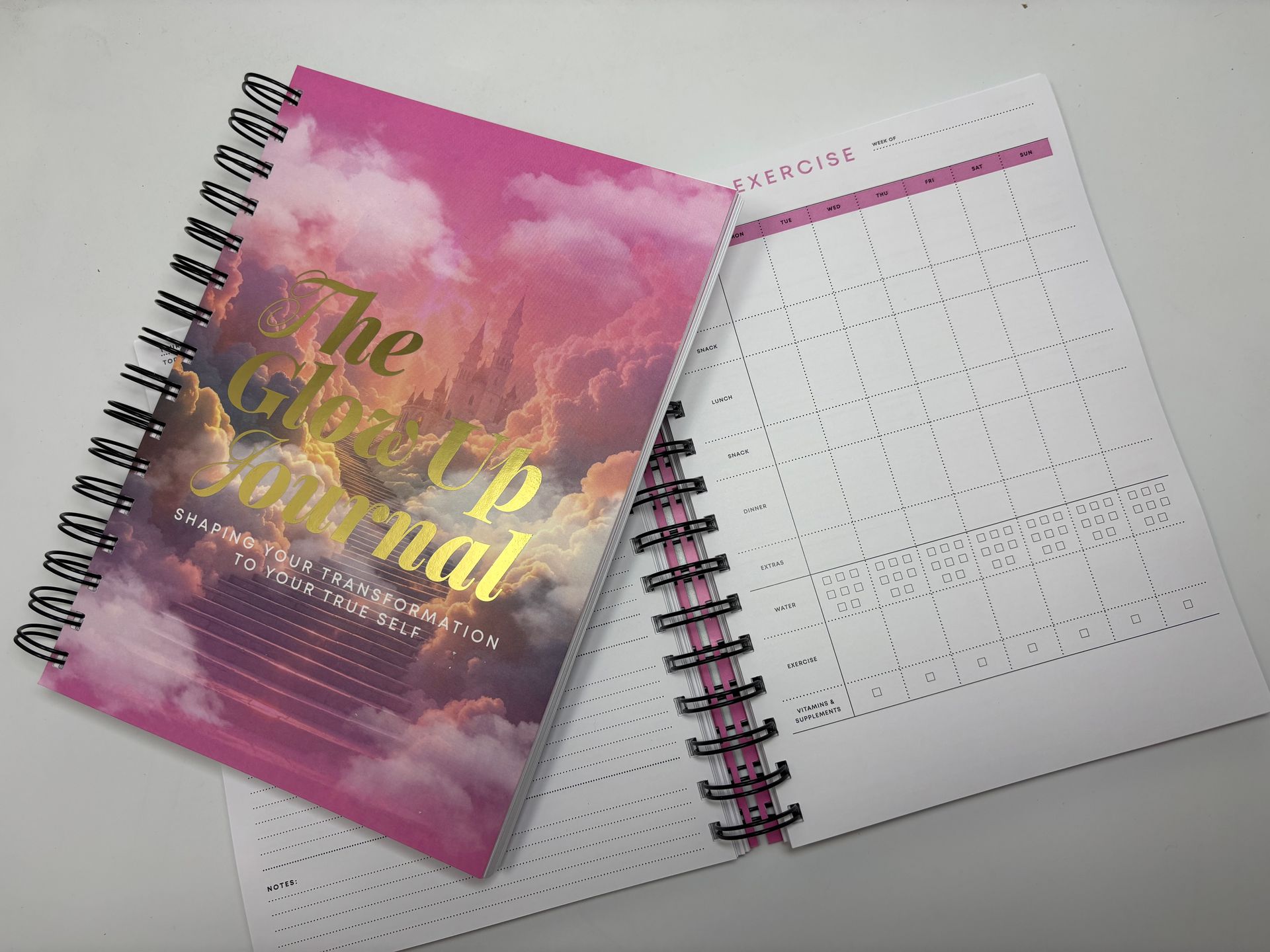 A spiral notebook with a pink cover is sitting on a table.