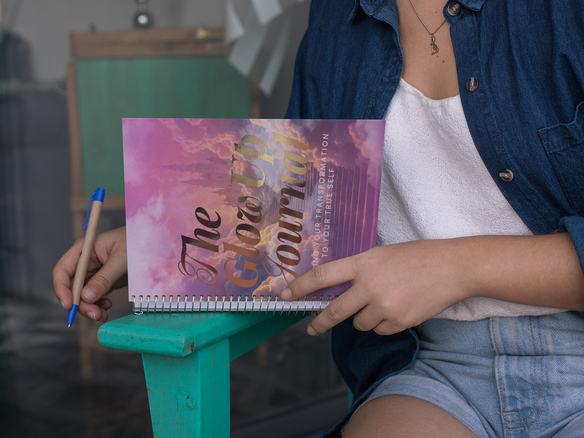 A woman is sitting on a chair holding a notebook and a pen.