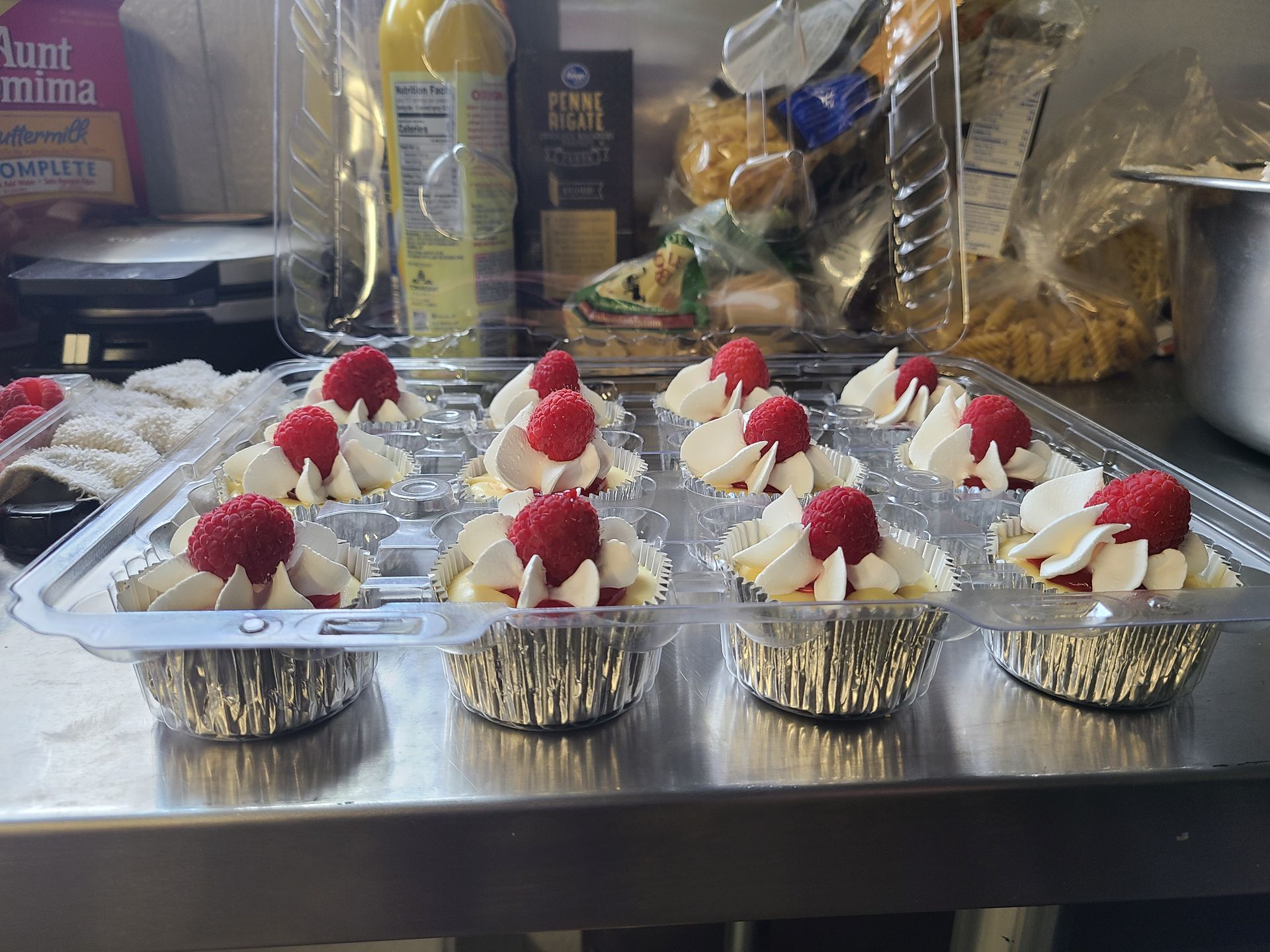 A tray of cupcakes with raspberries and whipped cream on top