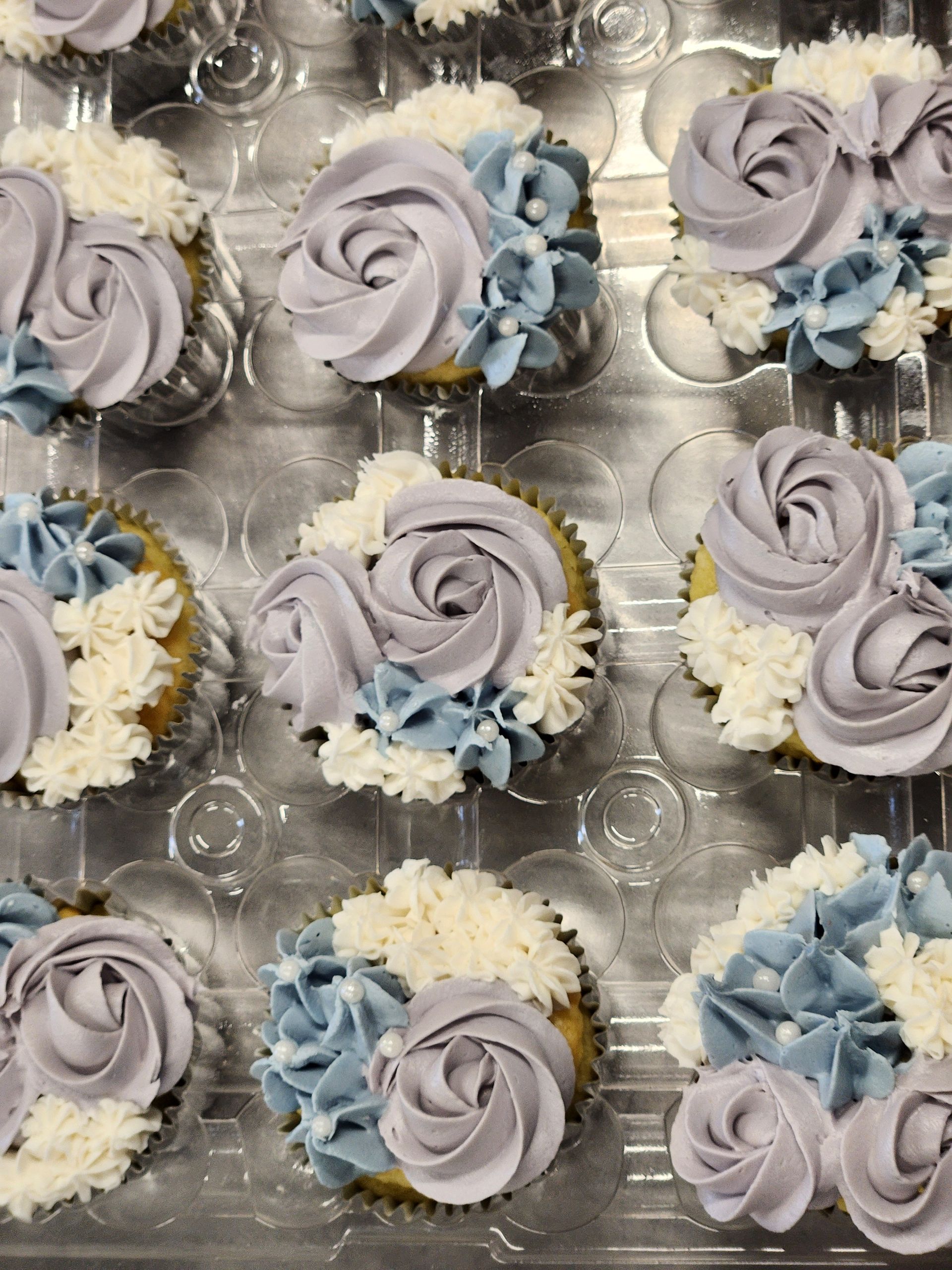 A tray of cupcakes decorated with purple frosting and blue flowers.