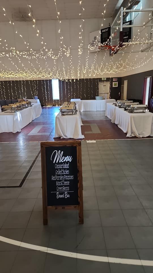 There is a chalkboard in the middle of a room with tables and a basketball hoop.