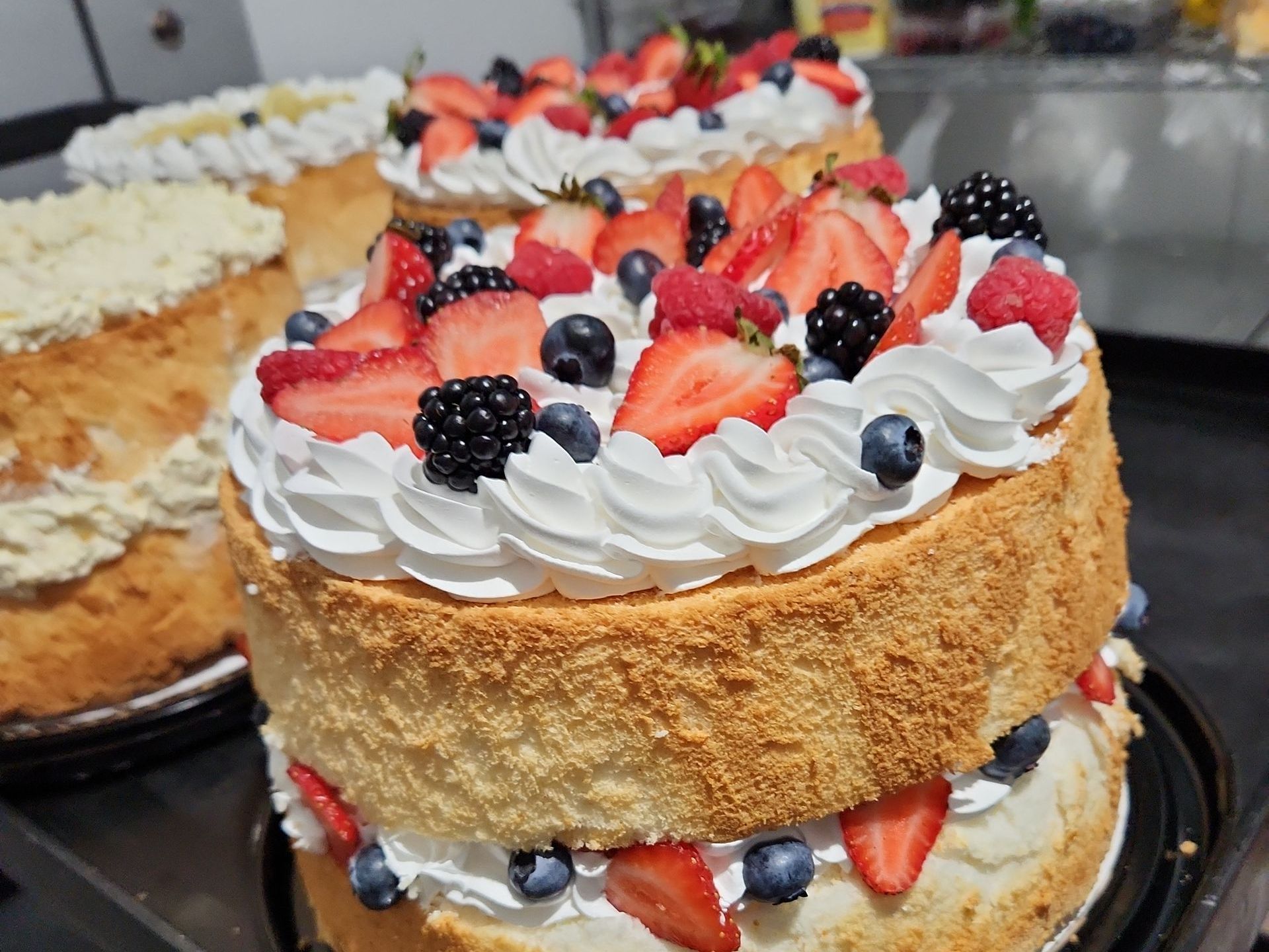 A cake with strawberries , blueberries , raspberries and whipped cream on top.