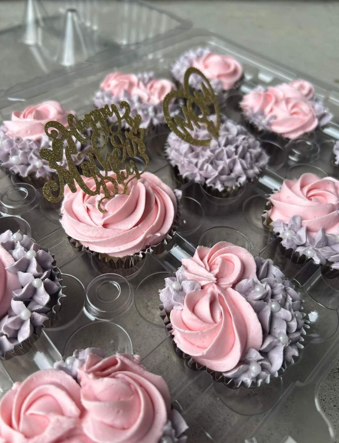 A plastic container filled with pink and purple frosted cupcakes.