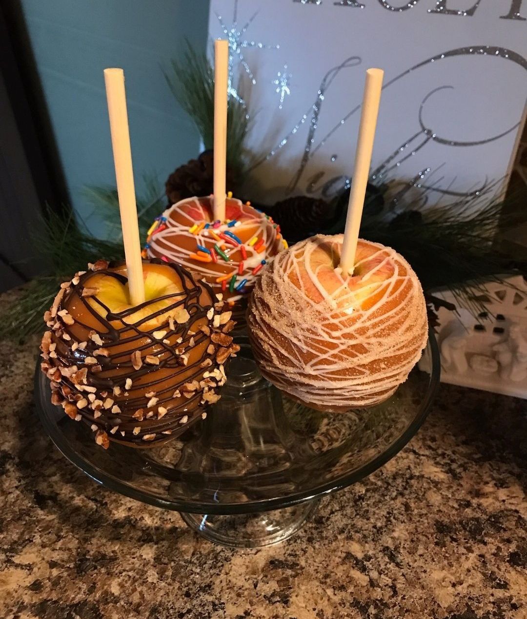 Three caramel apples are sitting on a glass plate on a counter.