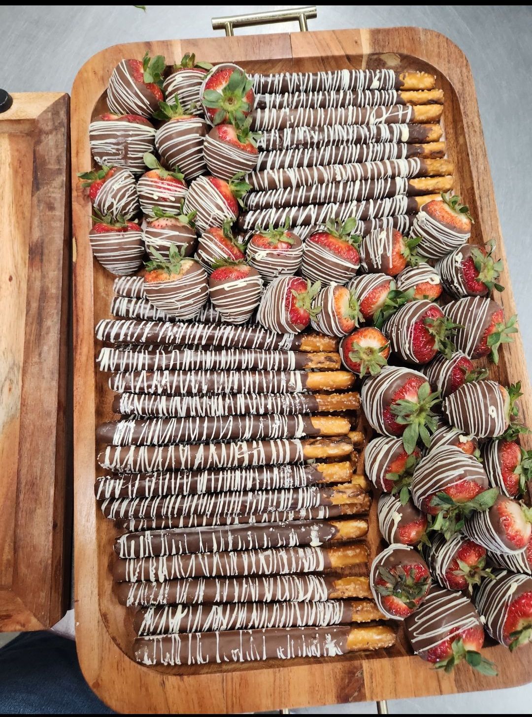 A wooden tray filled with chocolate covered strawberries and pretzels.