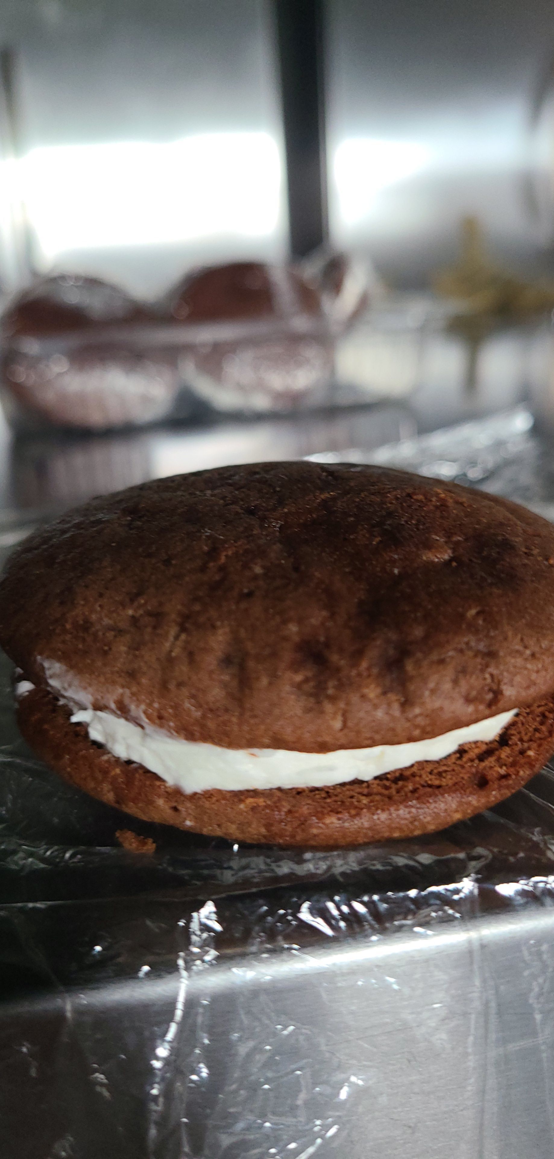 A close up of a chocolate sandwich with whipped cream on a metal surface.