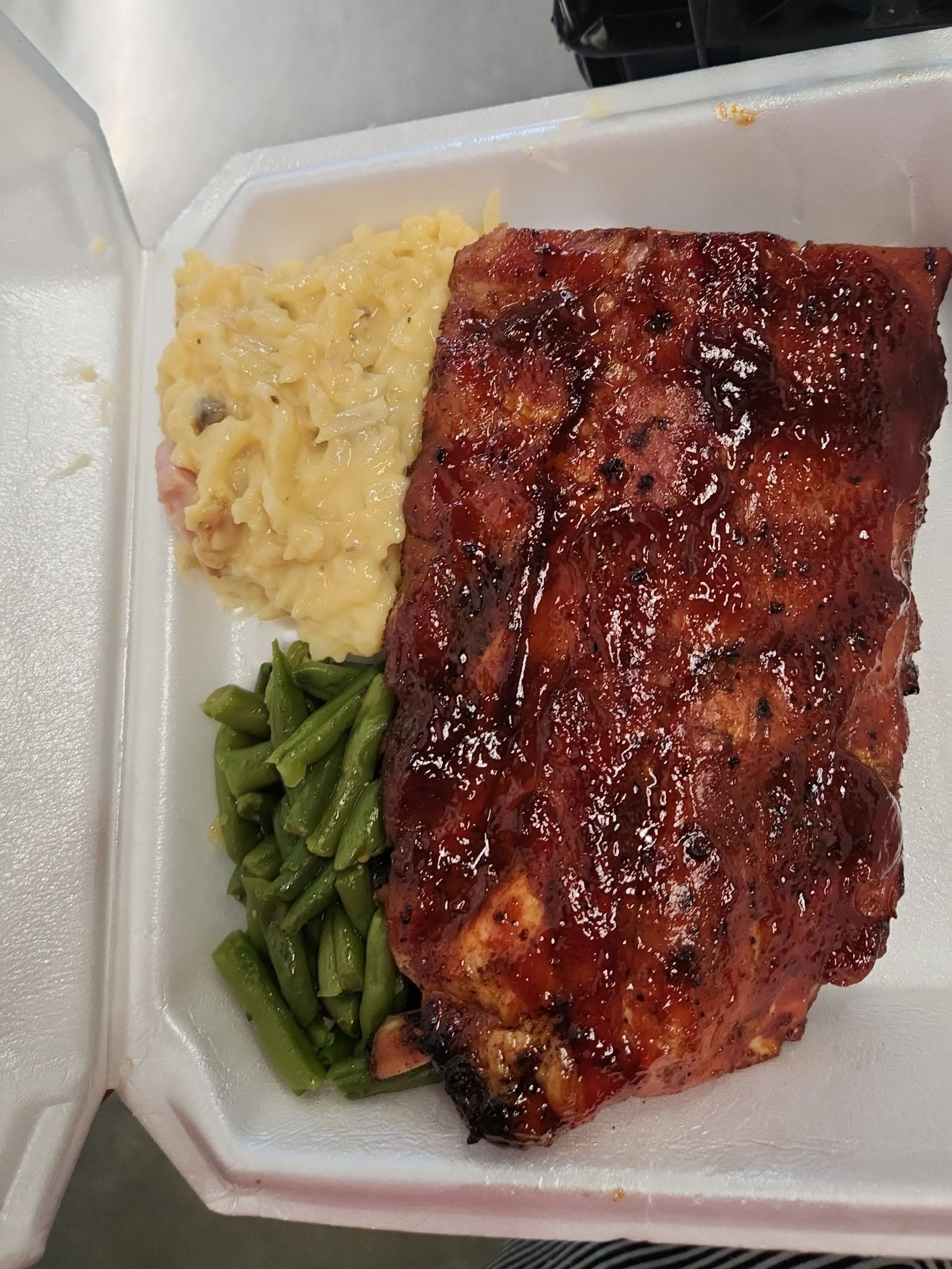A styrofoam container filled with meat , green beans and mashed potatoes.