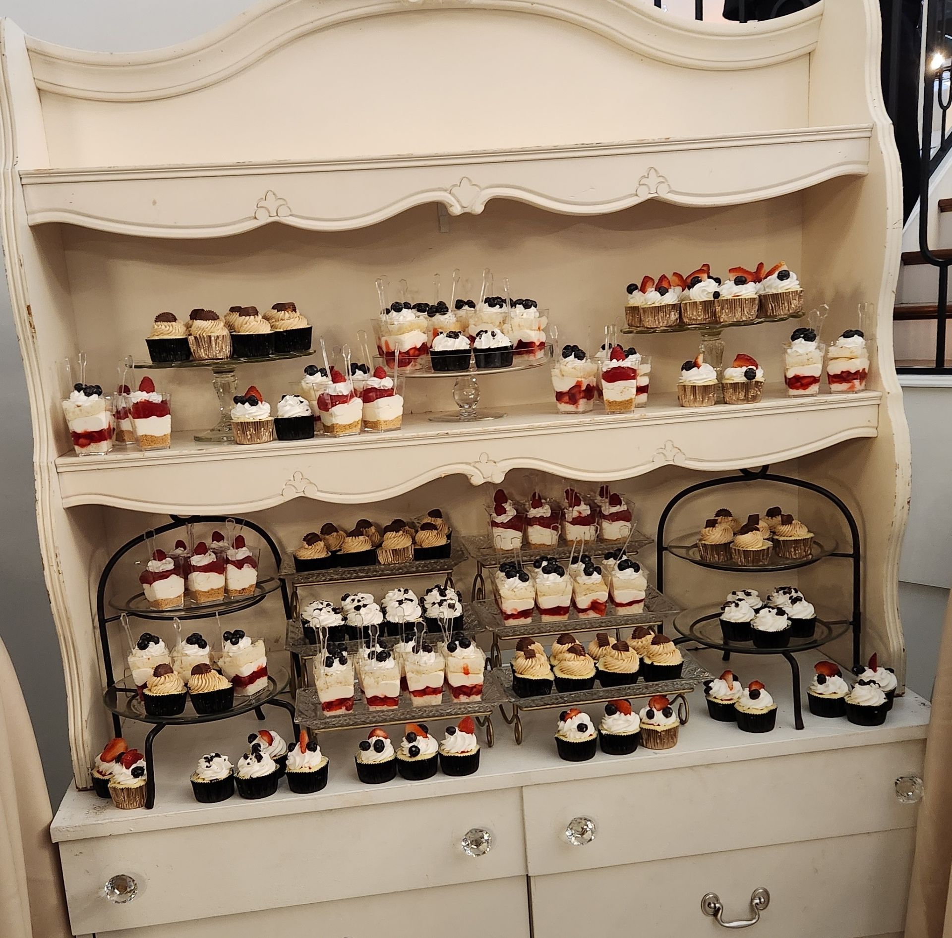 A white hutch filled with lots of cupcakes on shelves