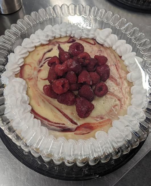A cheesecake with raspberries and whipped cream on top