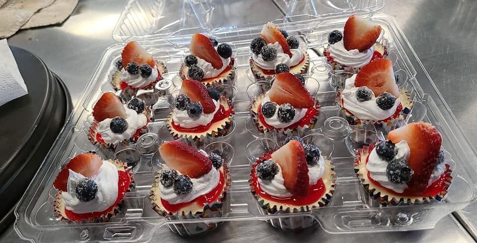 A plastic container filled with cupcakes with strawberries and blueberries on top.