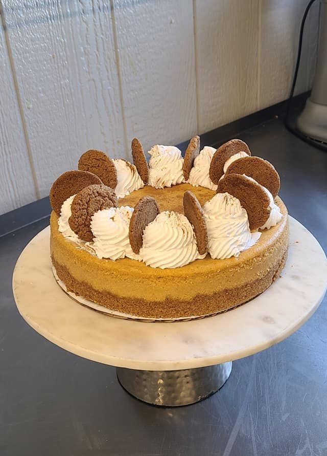 A pumpkin cheesecake with whipped cream and gingerbread cookies on a marble cake stand.