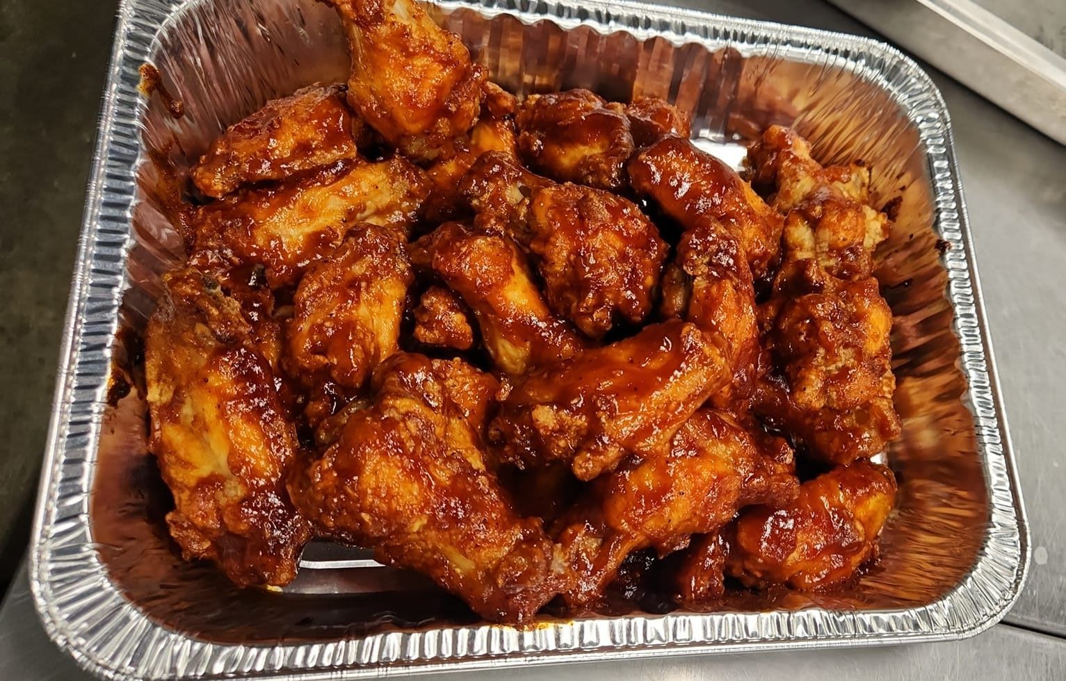 Aluminum foil tray filled with fried chicken wings covered in sauce.