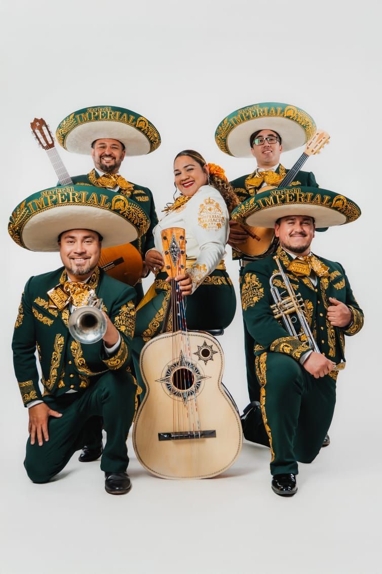 Un grupo de mariachis de cinco integrantes, vestidos con trajes verdes y dorados a juego y grandes sombreros