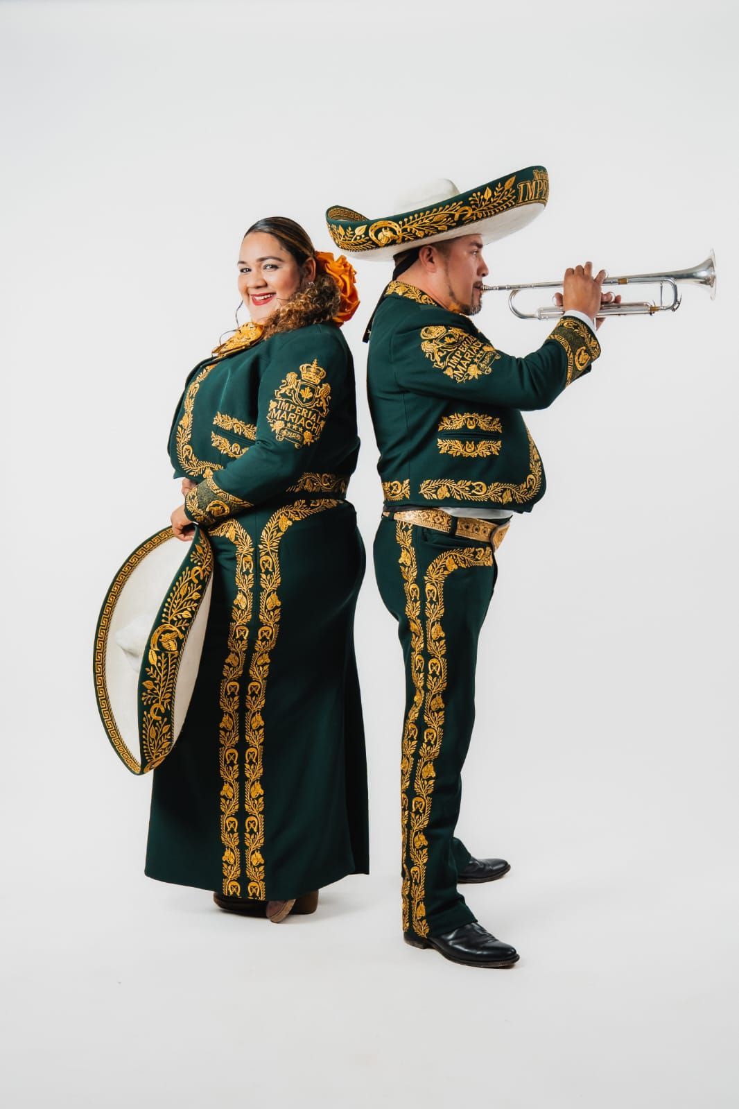 Dos músicos de mariachi con trajes verde oscuro bordados en oro posan de espaldas