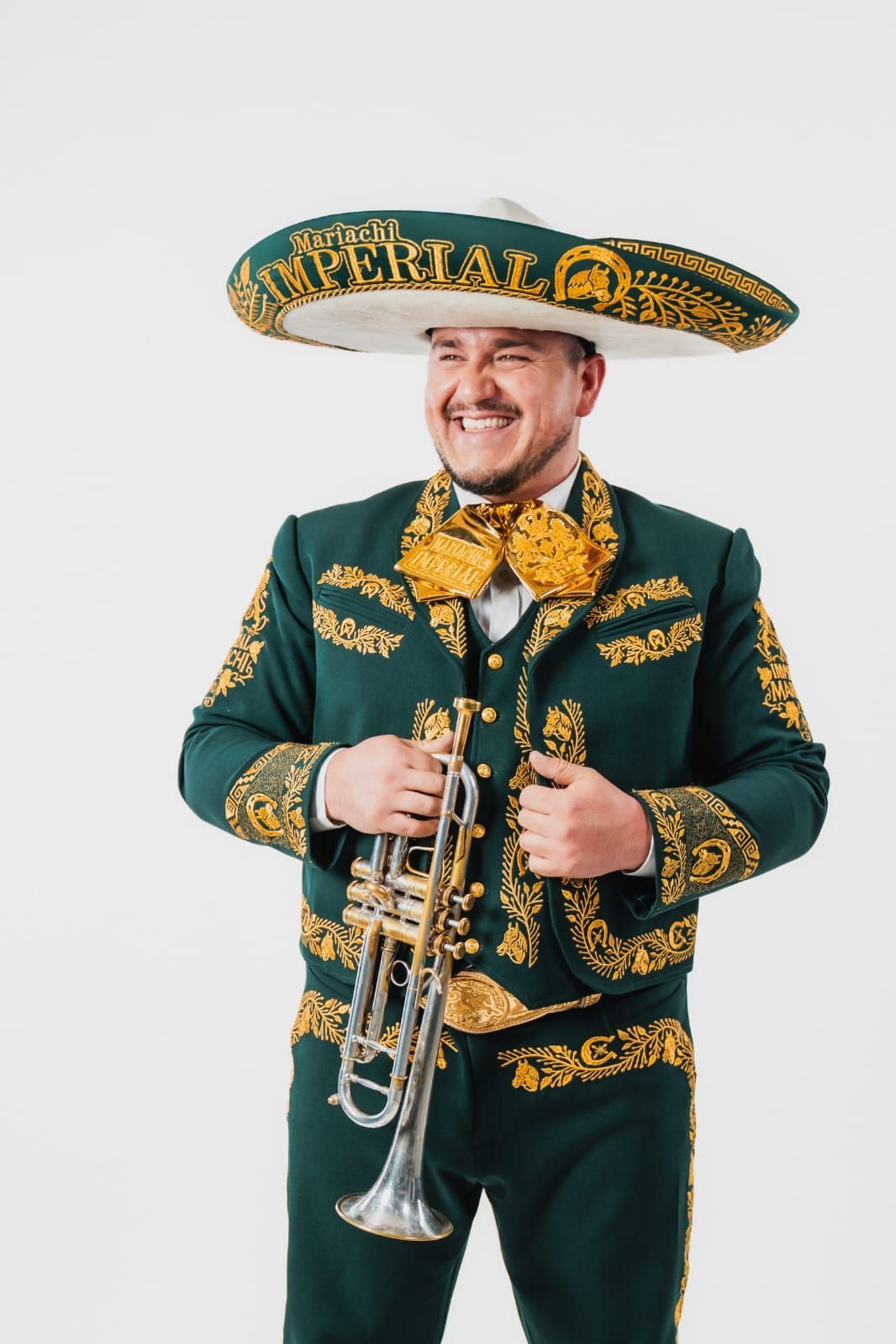 Un músico sonriente viste un traje de charro verde oscuro con bordados dorados y un sombrero de ala ancha