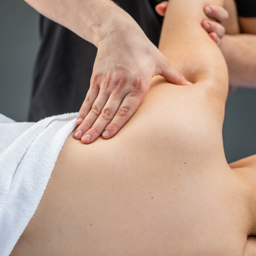 Person receiving massage on their upper back and shoulder, therapist's hands applying pressure.