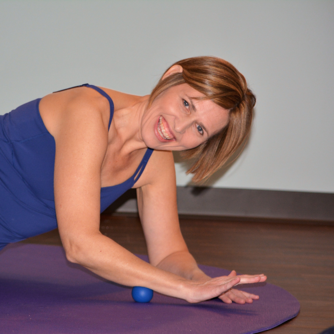 Woman exercising on a purple mat, using a blue ball, smiling.