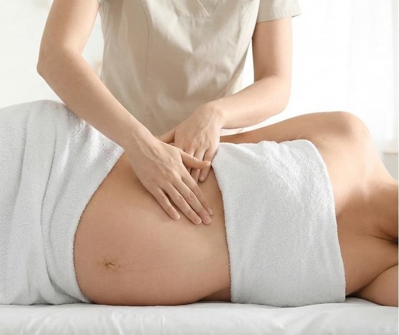 A person in a light blue shirt is lying down on an examination table. A person with dark skin is touching their abdomen.