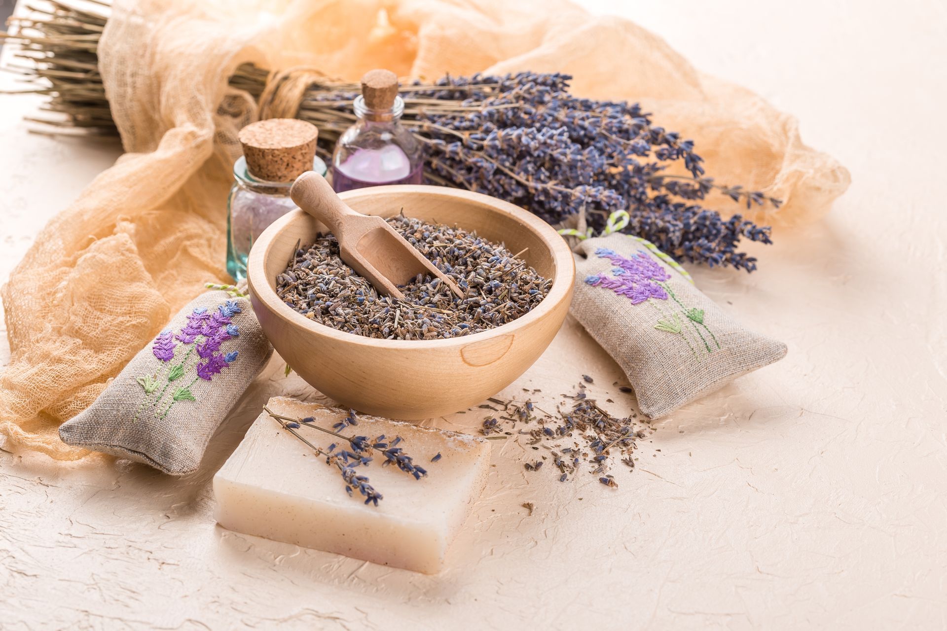 Lavender arrangement: dried flowers, soap, oil bottles, potpourri in a wooden bowl, linen sachets.