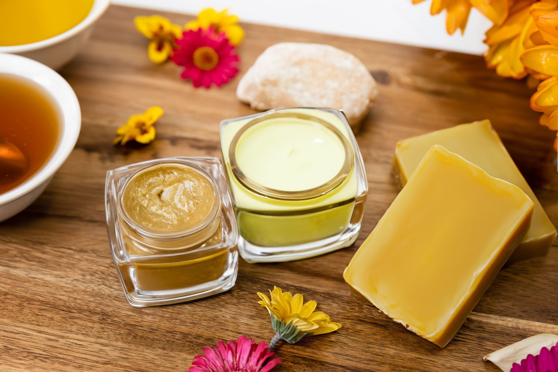 Jars of cream and soap bars on a wooden surface with tea and flowers.